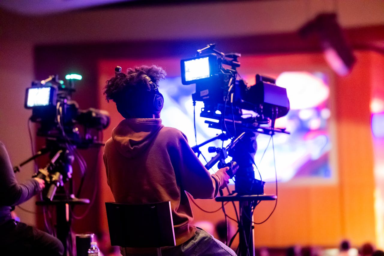 hero-img-02 Back view of a videographer operating a camera at a live event, focusing on a vibrant indoor setup.